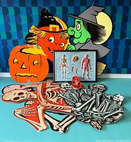 Photo showing colorful vintage cardboard Halloween decorations and some skeleton figures laid out on a surface.