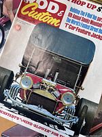 Close-up photo of vintage Rod & Custom magazine featuring a red vintage hot rod with a prominent V8 engine and visible wear on cover
