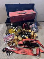 Overall view showing vintage red Snap-On toolbox inside a larger black plastic toolbox, with multiple tie down straps placed in front.