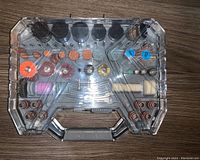 Closed transparent case containing multiple drill accessory attachments organized inside.