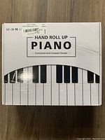 Box with product branding reading 'Hand Roll Up Piano - Functional and Compact Design', showing part of piano keys design.