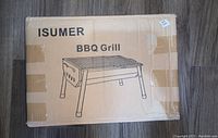 ISUMER BBQ Grill cardboard box with image and brand, sealed with brown tape, showing product illustration.