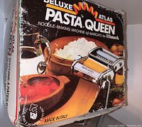 Box front of Deluxe Pasta Queen Atlas noodle-making machine showing image of the machine, pasta ingredients, and branding with Made in Italy