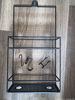 Full view of black metal shower head caddy with three metal hooks separated inside the frame