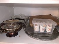 Silver-plated serving items including a tray with handle and pedestal bowl, clear glass bowl, and plastic container with spice jars on shelf.