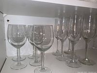 Photo showing 5 wine glasses and 6 champagne glasses arranged in two rows on a white shelf.