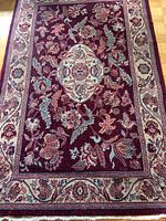 Full view of the carpet showing the central medallion, floral patterns, and wide border with flowers on a burgundy background.