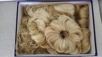 Box containing multiple blonde hair attachments, loosely arranged with varied shades of blonde showing wavy curls and volume.