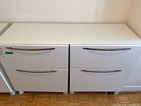 Photo showing two white IKEA Besta cabinets side by side with two drawers each and curved silver metal handles.