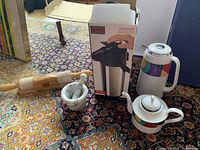 Photo showing Oggi Pumpmaster carafe box, wooden rolling pin, marble mortar and pestle, and Mikasa teapot and carafe with colorful band.