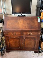Front view of closed wood secretary desk cabinet with drop-down desk closed; shows wood grain, brass handles, and scratches.