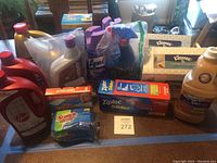 Photo showing multiple cleaning supplies on table including Swiffer Wet Jet, Lysol spray cans, Kleenex hand towels, Ziploc bags, and others.