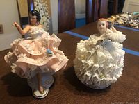 Two Dresden lace porcelain figurines displayed side by side on a table.
