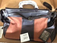 Front view of two-tone dark brown and rust colored leather handbag with zipper closure and attached transparent ID or luggage tag pouch.