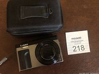 Front view of Lumix camera with attached lens and carrying case behind