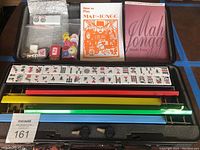 Top-down photo showing the lockable black case containing arranged mah-jongg tiles, colored tile racks in red, yellow, green, and blue, instruction booklets, and chips.