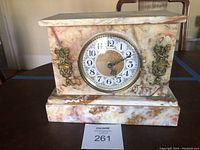 Front view of veined marble mantle clock showing rectangular marble housing with natural veining and golden decorative pieces on corners.
