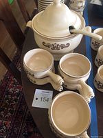 Soup tureen with lid and ladle alongside six French onion soup bowls showing the brown floral pattern.