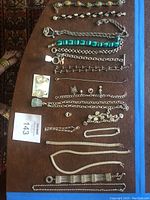 Complete set of silver tone costume jewelry laid out on brown surface with variety of bracelets, necklaces, earrings, and charms in chain link and bead form.