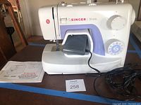 Full side view of the Singer Simple sewing machine with the foot pedal connected and instruction manual in front.