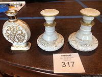 Photo of three vintage hand painted French porcelain perfume bottles in white with intricate gold decoration, including one flat circular bottle with geometric base and two round base bottles with matching stoppers.