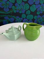Front and side view of the green Bauer pitcher and light green Hall teapot displayed on white surface with floral background