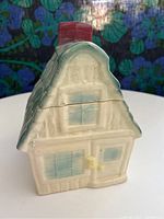 Front view of farmhouse cookie jar showing cream color body with blue window panes, yellow door details, and red chimney