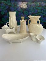 Full lot display of eight vintage white pottery pieces showing varied shapes and embossed decoration.