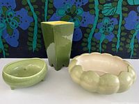 Front view showing all three pieces: tall angular vase, scalloped round pot, and oval pot with feet.