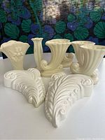 Photo displaying six vintage cream-colored pottery vases with varied fluted and scroll shapes arranged on a table.