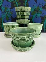 Photo showing the four McCoy vintage ceramic pots in green shades with their saucers, highlighting their embossed textures and patterns.