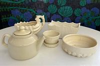 Photo of five cream glazed McCoy pottery pieces showing a teapot, swan-handle pot, planter, scalloped bowl and smaller pot.
