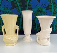 Front view of three vintage McCoy vases including yellow double-handled floral relief vase, plain tall pedestal vase, and spiral design vase.