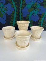 Front view of 4 vintage Shawnee glazed ceramic planters with matching saucers, cream color with embossed decorative patterns