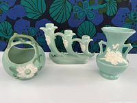 Three vintage green Weller Pottery Cameo & Dogwood items on a white surface against a floral backdrop, showing front and side views.