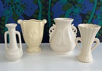 Front view of 4 ceramic vases in cream and yellow glazes showing various handle styles and shapes.