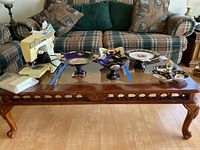 Wood and glass coffee table with sewing machine and decorative plates on top, viewed from front angle showing carved apron and cabriole legs.