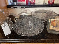 Overall photo showing glass bowl, vase, cake stand, plates and small glass creamer on countertop