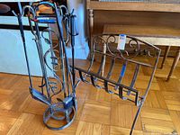 Photo showing the full set of black wrought iron fireplace tools including poker, tongs, shovel, and brush next to the wildlife holder on a hardwood floor.