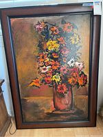 Full view of framed floral painting with colorful flowers in vase and artist signature at bottom right.