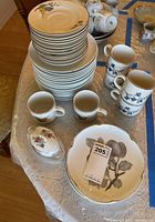 Photo showing stacked plates, coffee mugs, saucers, and a covered sugar bowl on lace tablecloth.