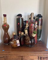 Front view of all ten decorative kitchen bottles arranged on wooden furniture showing various sizes and liquid infusions