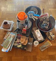 Assorted kitchen items laid out on floor including electric juicer, baking trays, wooden utensils, graters, cups, and small packaging boxes.