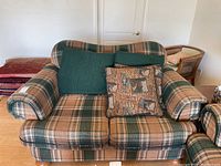 Front view of loveseat showing green and tan plaid pattern, two green cushions, and two wildlife patterned throw pillows.