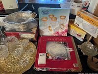Overview photo showing multiple glassware items including platters, boxes, cups with gold rim, and candy dishes arranged on a table