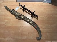 Full view of curved brass scabbard and wooden display stand on wooden floor