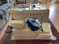 Front and side view of the cream-colored Singer 1802 sewing machine placed on a table with power cord visible.