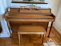 Front view of Lowrey spinet upright piano with matching bench in light brown wood finish.