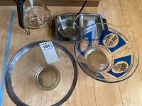 Overview of coffee decanter, metal rimmed glass bowl, blue-patterned glass bowl, and metal serving tray with spoon on wooden table.