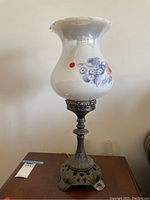 Full view of lamp showing porcelain floral shade and ornate brass base on wooden table.